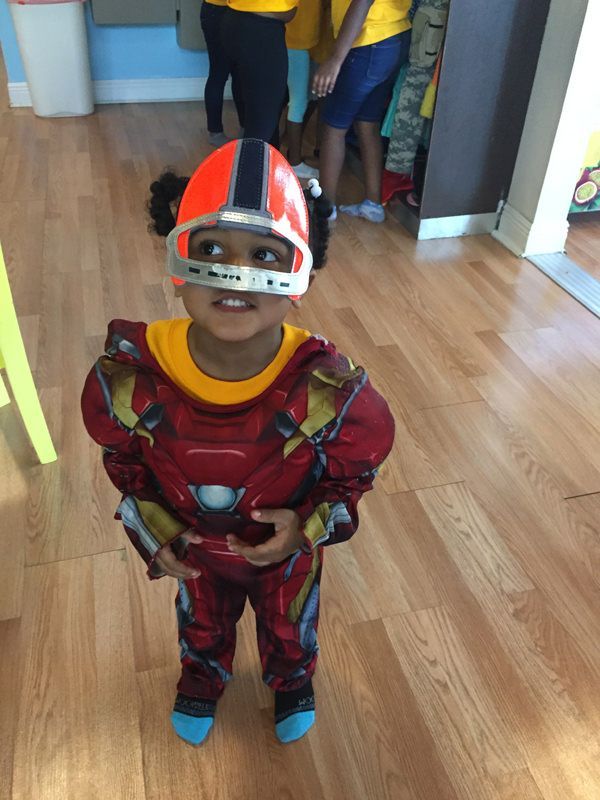 A young boy in a superhero costume is standing on a wooden floor.