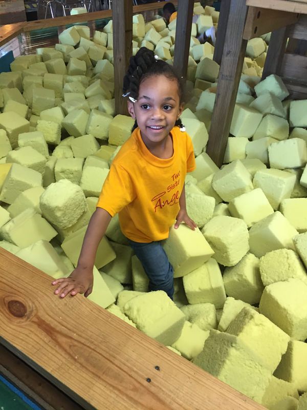A little girl in a yellow shirt is standing in a pile of foam cubes