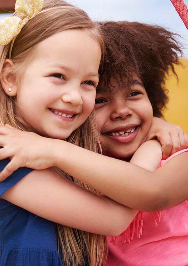 Two little girls are hugging each other at a playground.