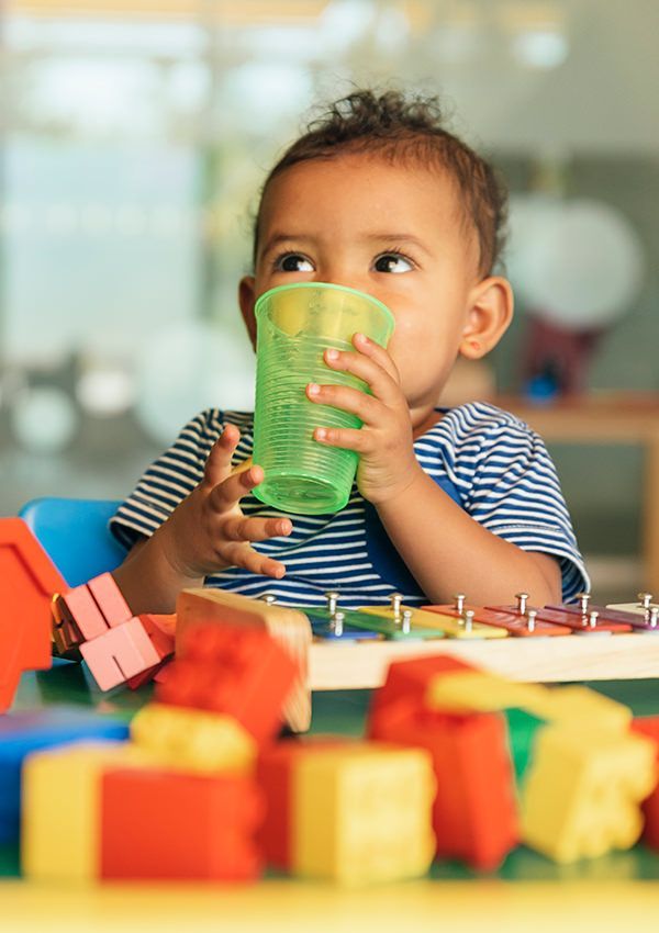 A baby is drinking from a cup while sitting at a table with toys.