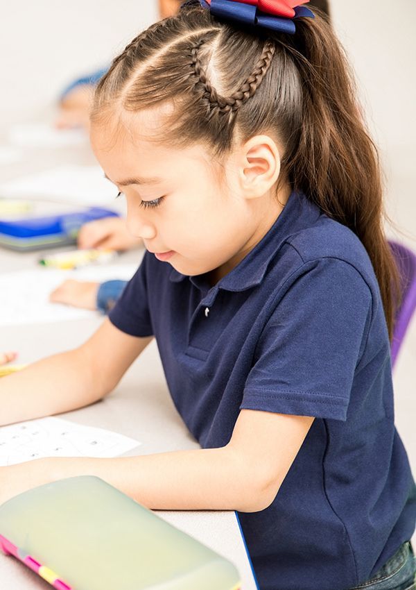 A little girl is sitting at a desk in a classroom.