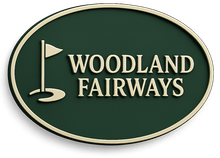 Oval sign for Woodland Fairways golf course, green background, gold border, and text with golf flag icon.