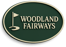 Sign for Woodland Fairways golf course, green oval with cream border and text, golf flag icon.