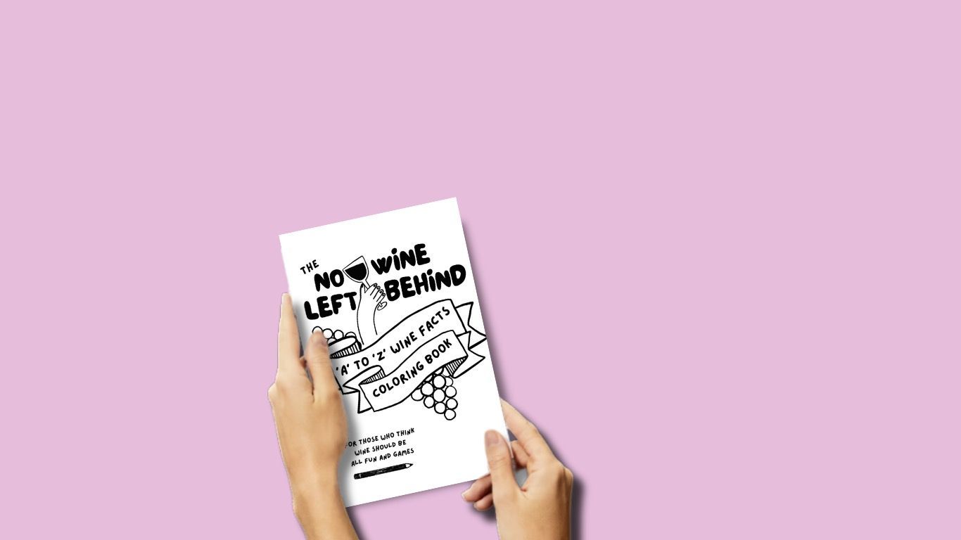 Two hands holding No Wine Left Behind’s interactive wine coloring book with a white cover and black design, titled “A to Z Wine Facts Coloring Book.”