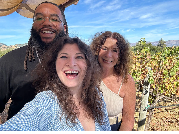Three people smiling in a sunny vineyard setting