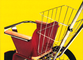 Red seat with basket attached to a bicycle. Yellow background.