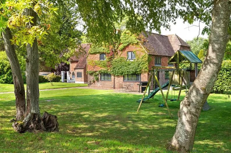 Brick house with green lawn and trees, with a wooden playset in the yard