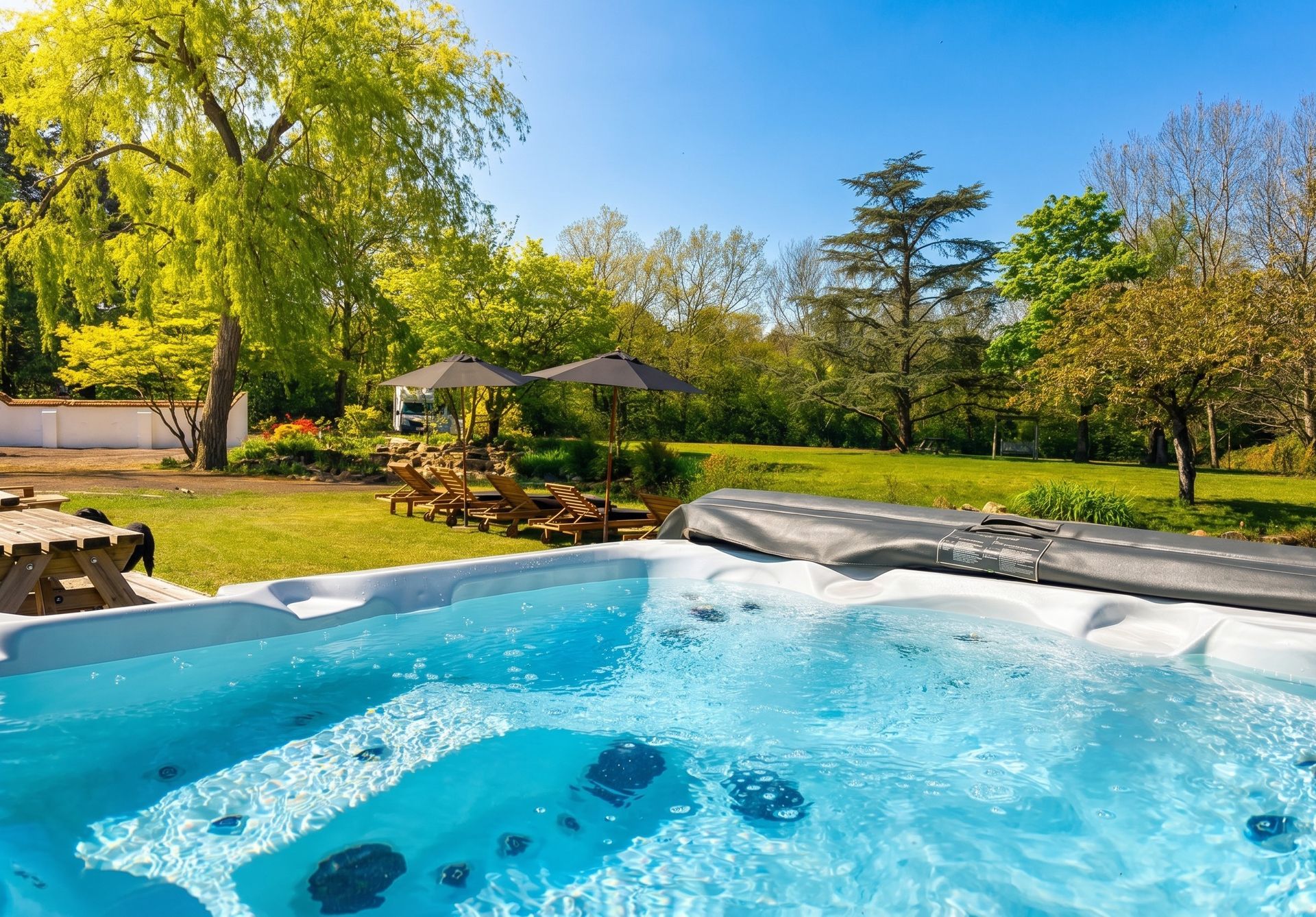 Blue hot tub with bubbling water in a sunny backyard garden with trees and lawn