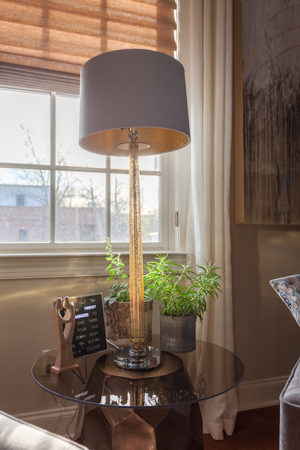 A lamp is sitting on a glass table next to a window.