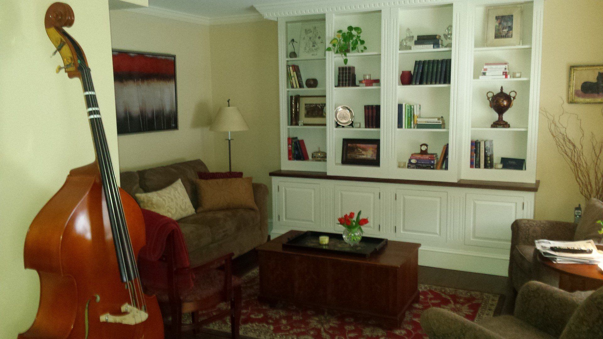 A double bass is sitting in a living room next to a couch.