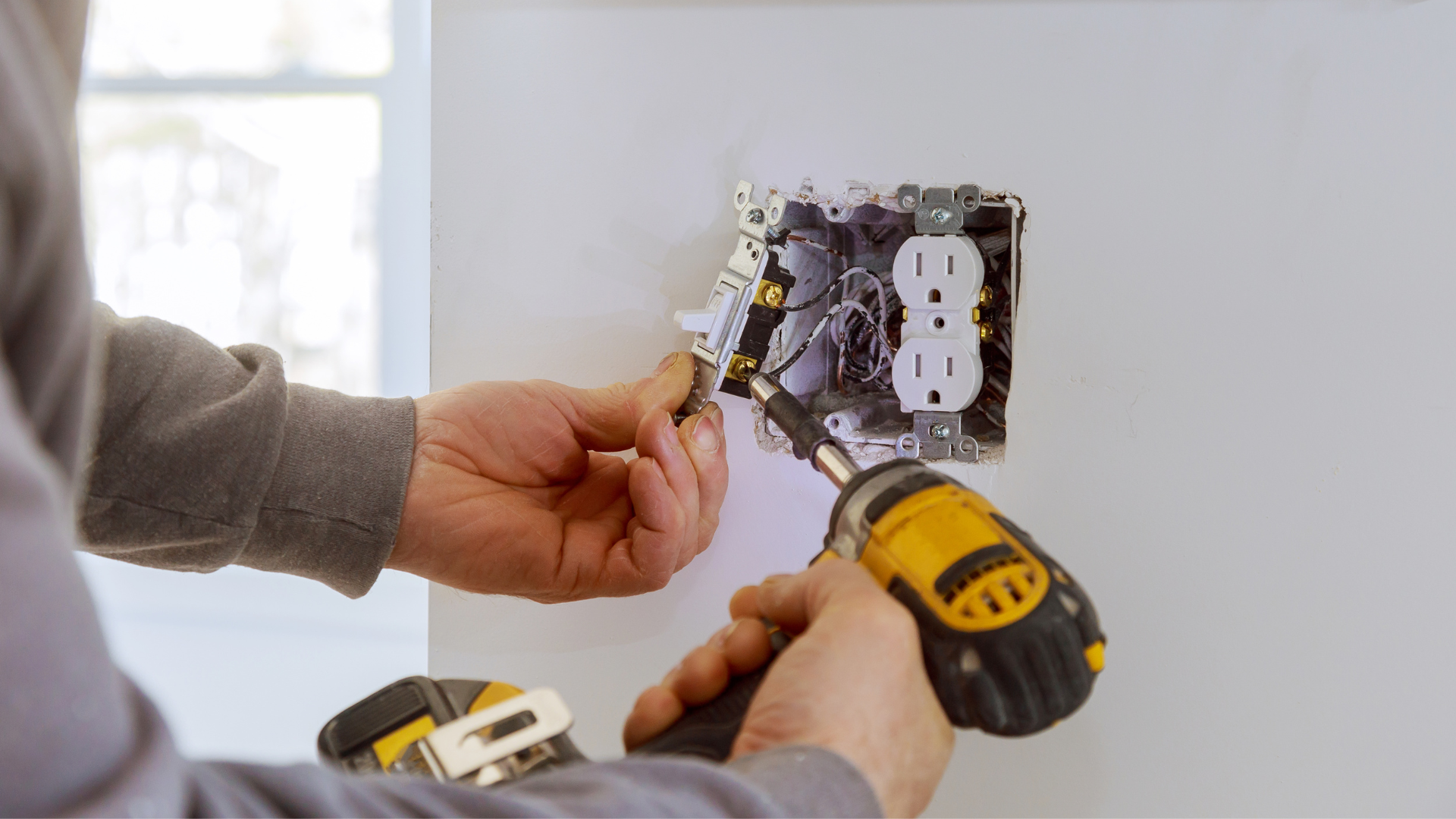 A man is using a drill to install an electrical outlet on a wall.