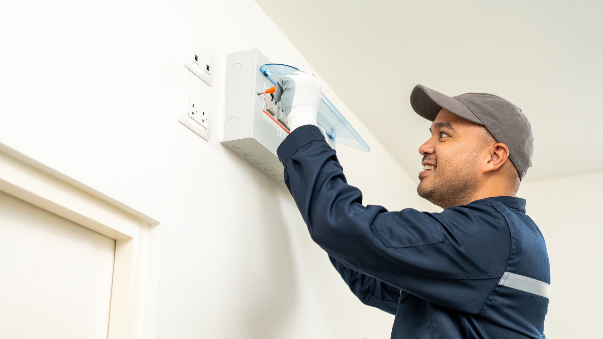 A man is working on an electrical box on a wall.