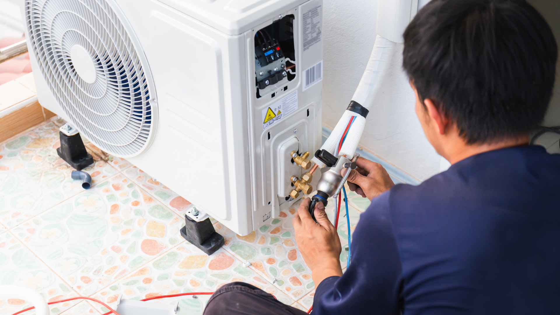 A man is sitting on the floor fixing an air conditioner.
