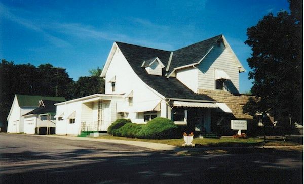 White building with a dark roof and small yard on a sunny day.