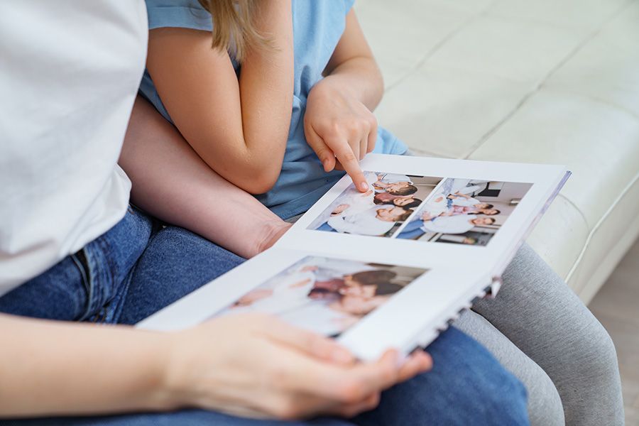 A person and child looking at photos in a photo album, pointing at a picture.