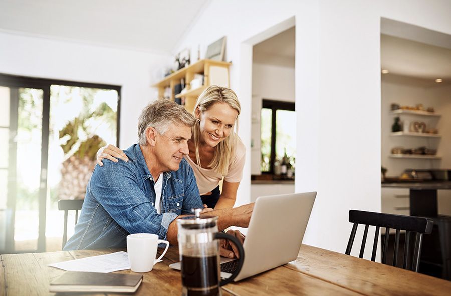 Man and woman looking at laptop together at a wooden table. The woman has her arm around the man.