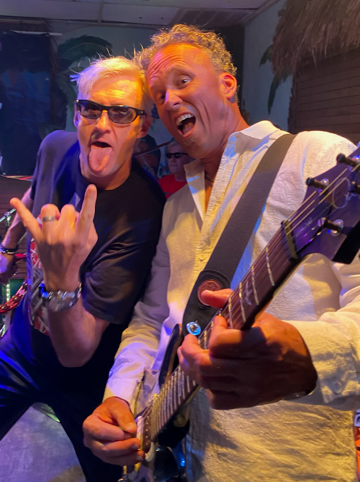 Two men are posing for a picture while one of them is playing a guitar.