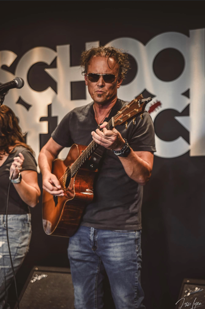 A man is playing a guitar in front of a sign that says school