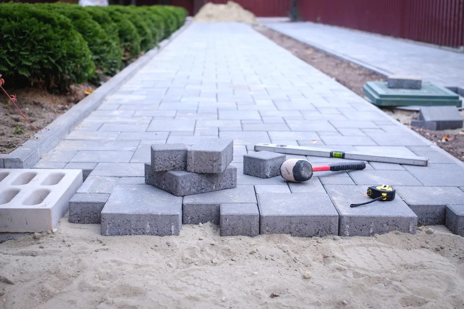 A sidewalk is being built with bricks and tools on the ground.