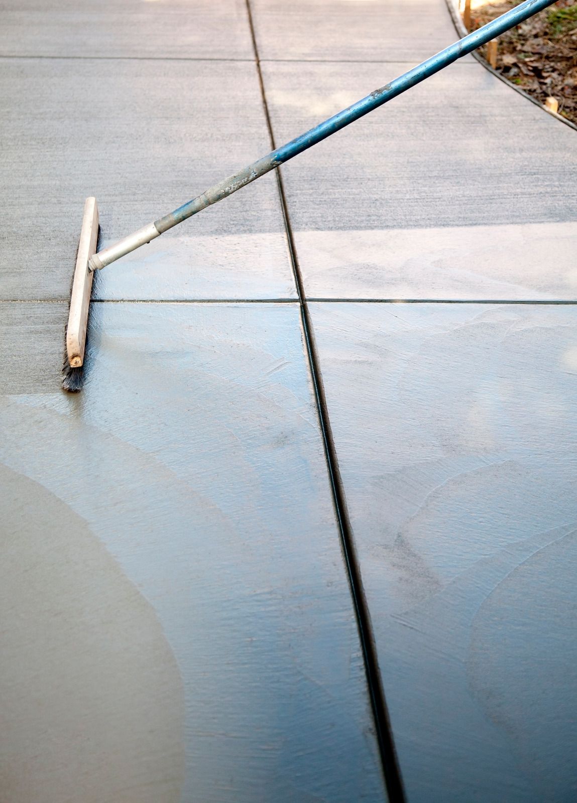 A person is using a broom to clean a concrete sidewalk.