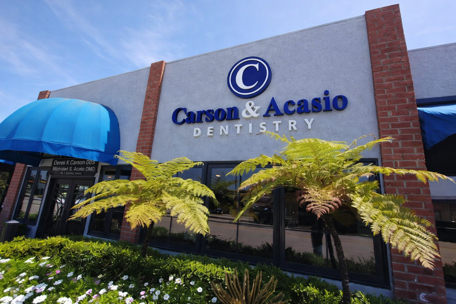 Carson & Acasio Dentistry storefront with blue awning, brick facade, and palm trees outside