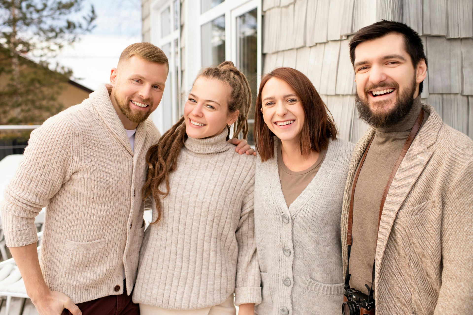 Four smiling adults in beige sweaters standing together outdoors by a light-colored building