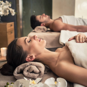 Two people receiving a relaxing spa massage with candles and flowers in a dimly lit room