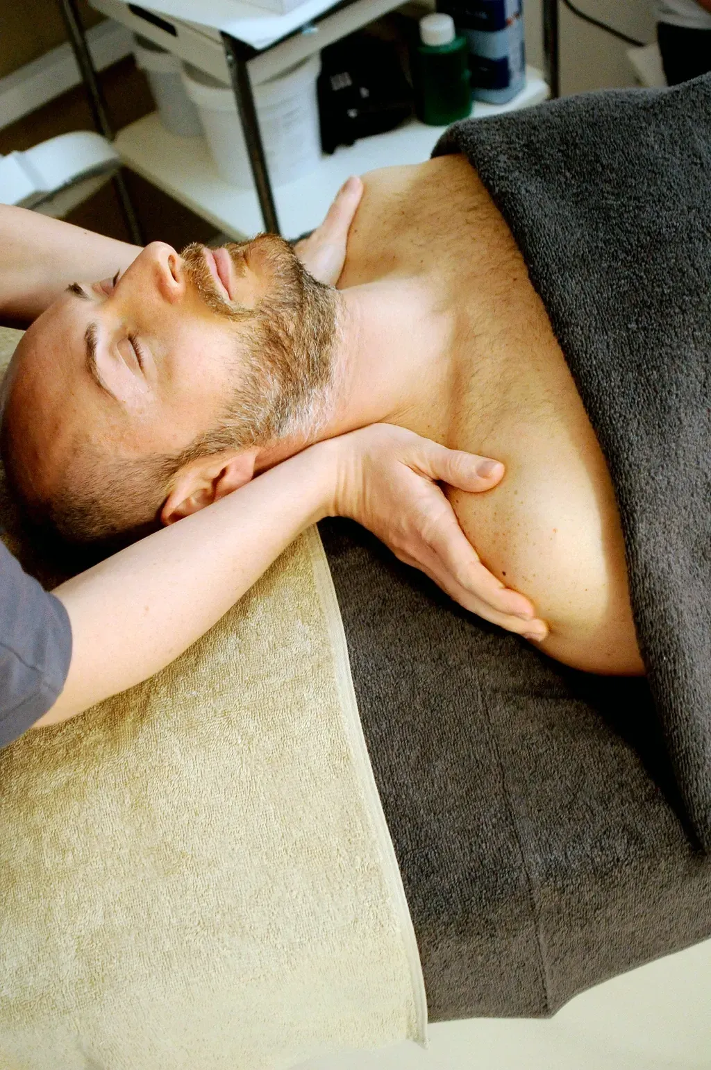 Person lying on a massage table while another person supports their head and neck in a spa setting