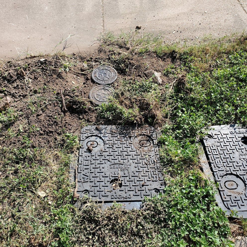 A manhole cover is sitting in the grass next to a sidewalk.