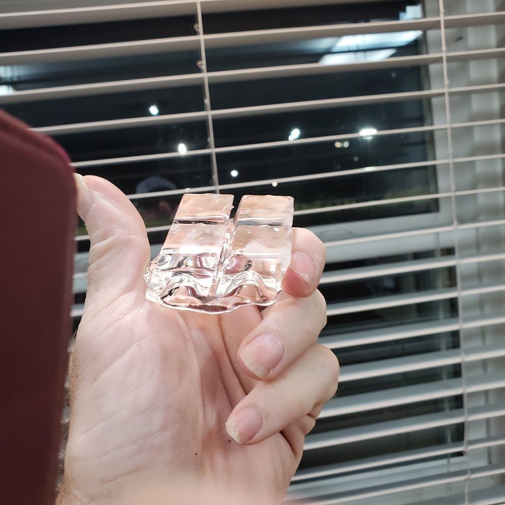 A person is holding two ice cubes in their hand in front of a window with blinds.