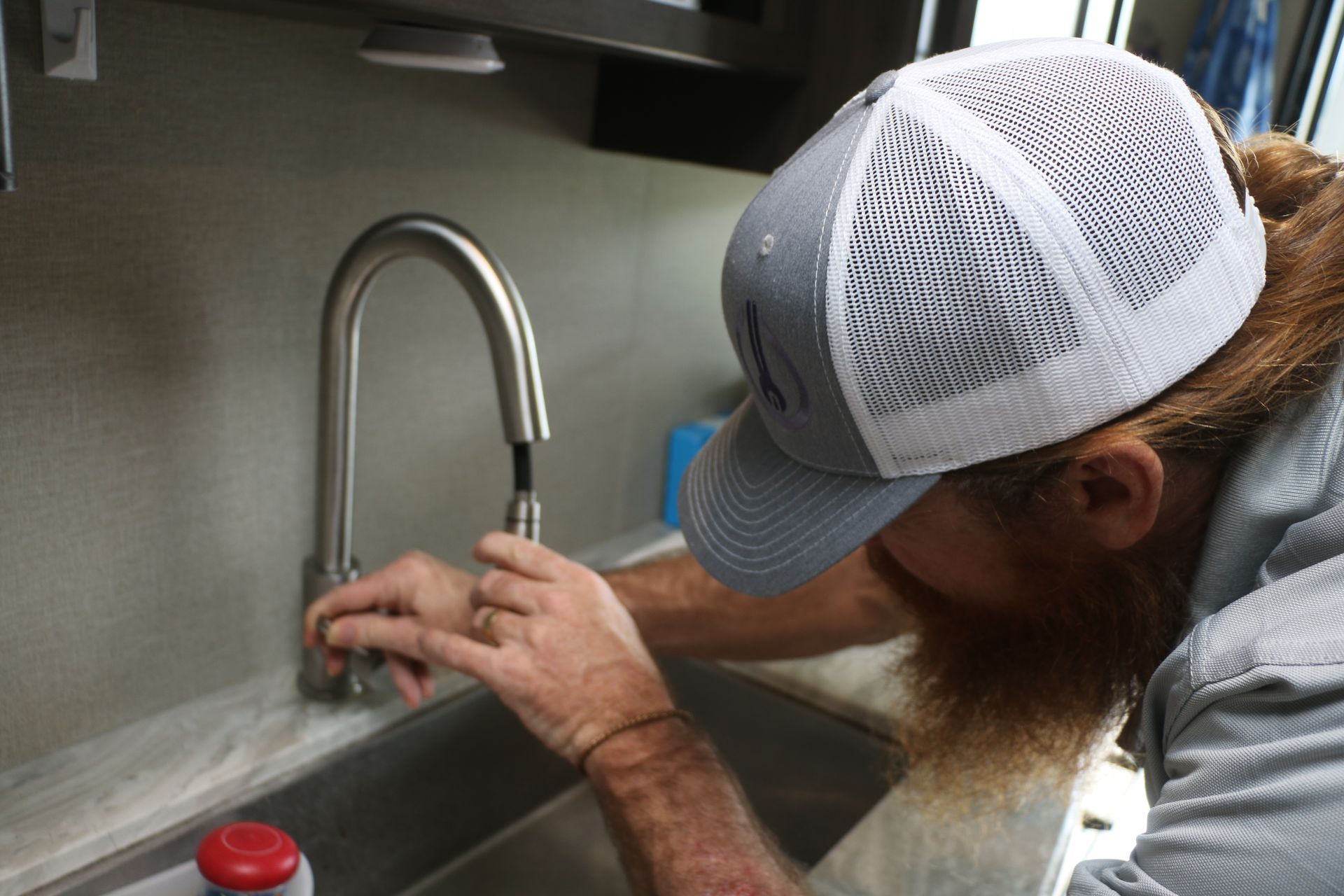 A man in a hat is fixing a faucet in a kitchen.