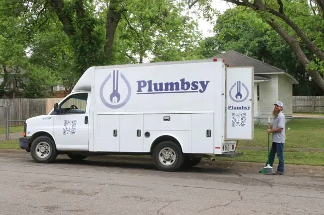 A white plumbing truck is parked on the side of the road