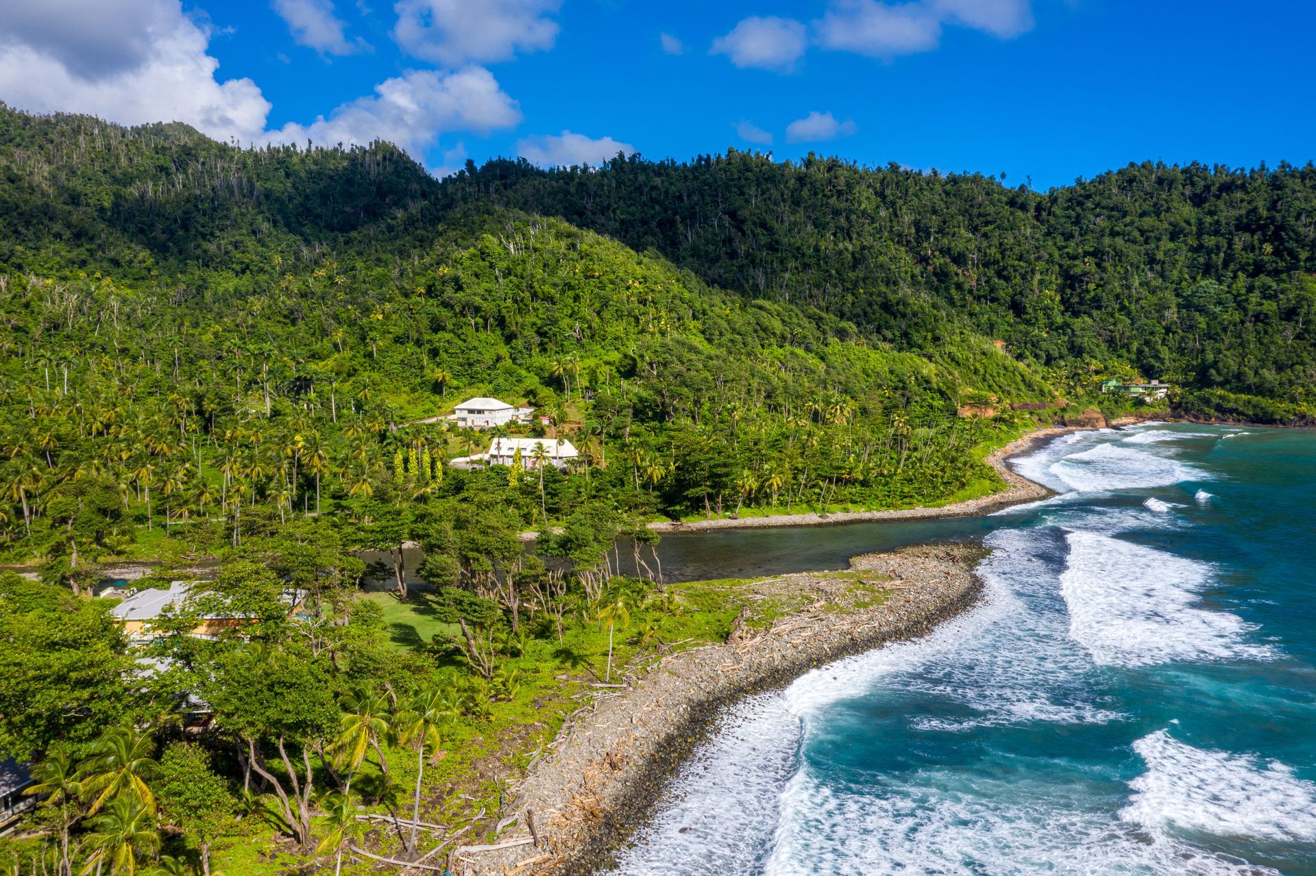 An aerial view of a tropical beach with mountains in the background and waves crashing on the shore.