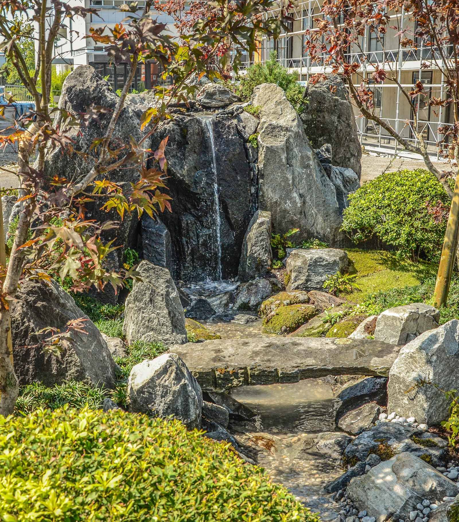 Una cascata è circondata da rocce e alberi in un giardino giapponese.