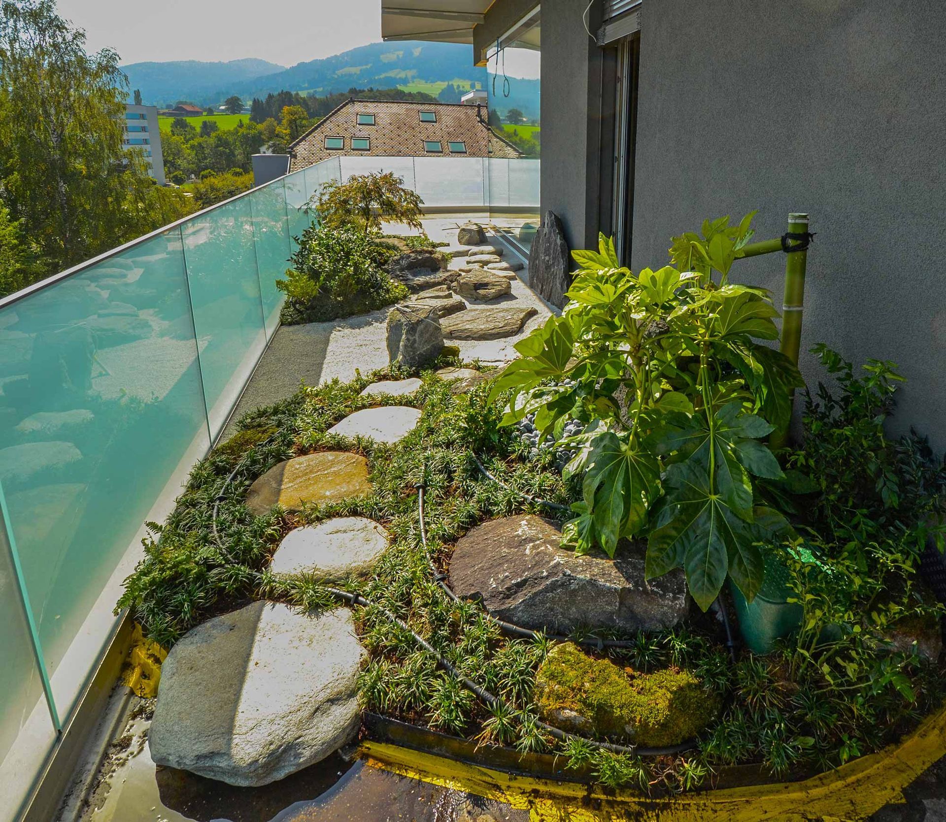 Un giardino con piante e rocce su un balcone con ringhiera in vetro