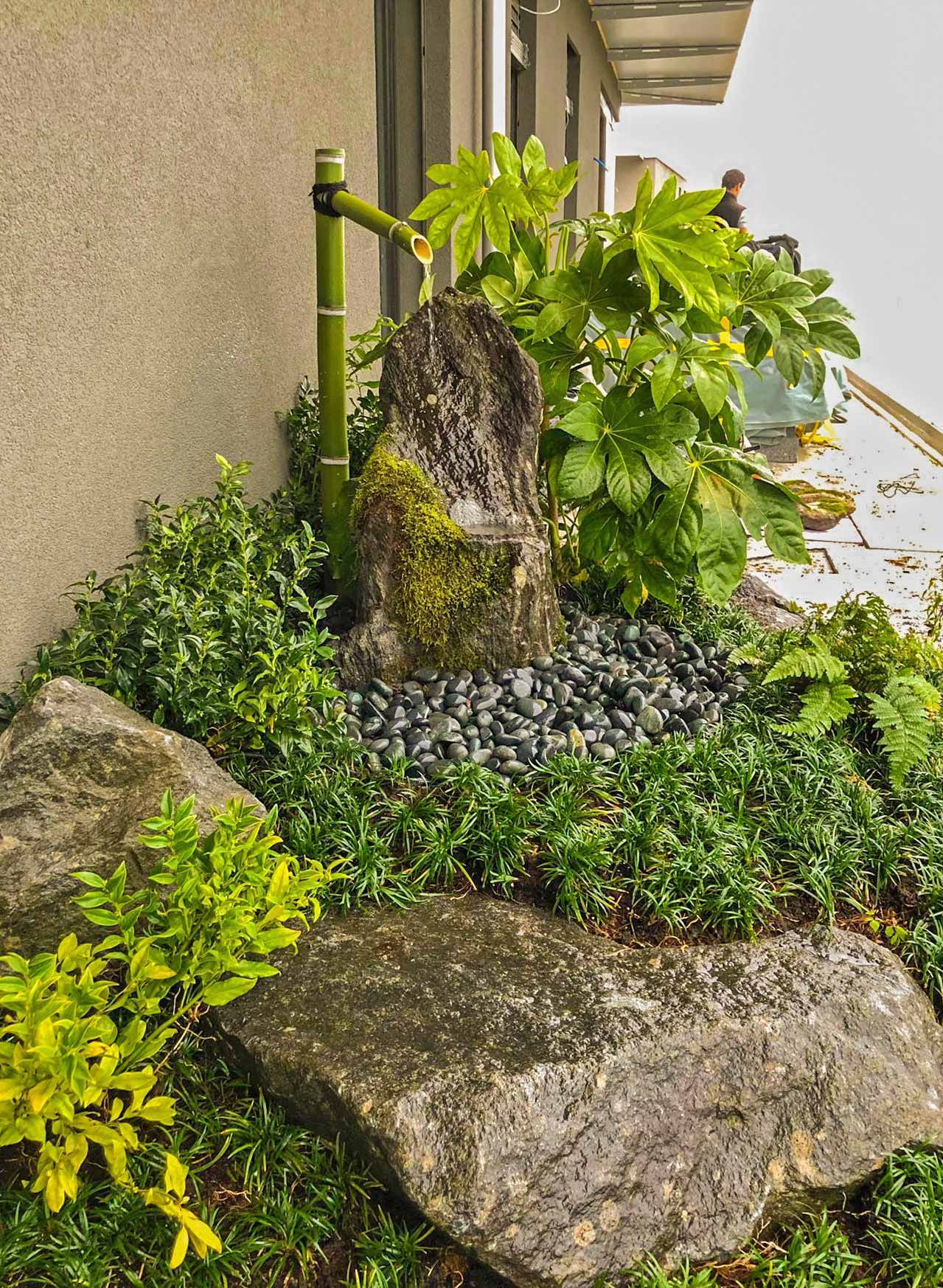Un giardino con rocce, piante e una fontana sulla terrazza di un edificio.