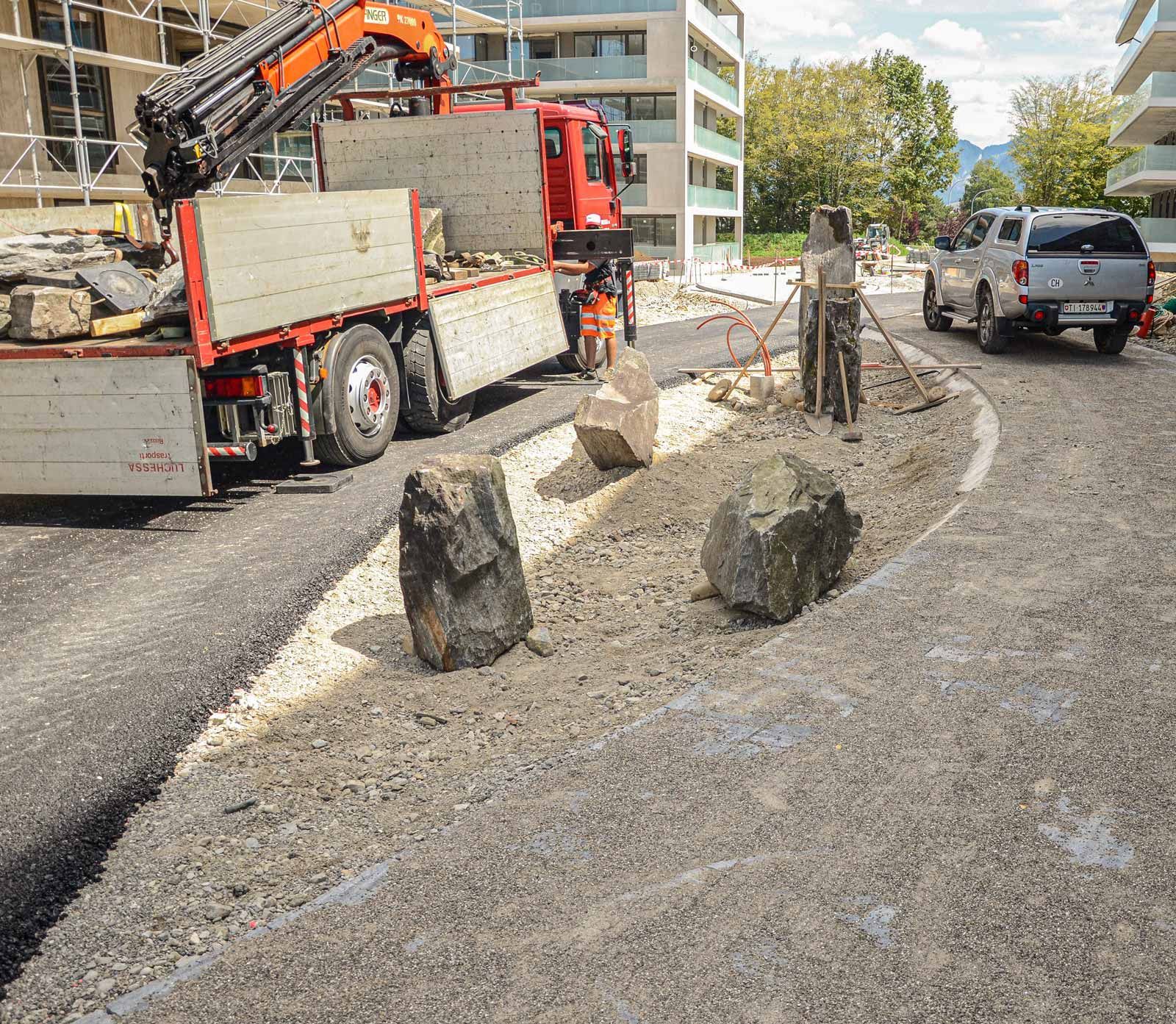 Un camion con una gru sul retro sta posando pietre in un'aiuola.