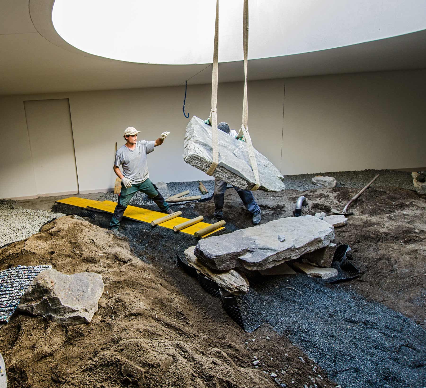 Due operai edili stanno sollevando una grande roccia in un cortile.