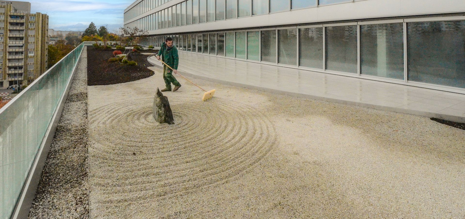 Un uomo sta rastrellando la ghiaia di un giardino zen sul tetto di un edificio.