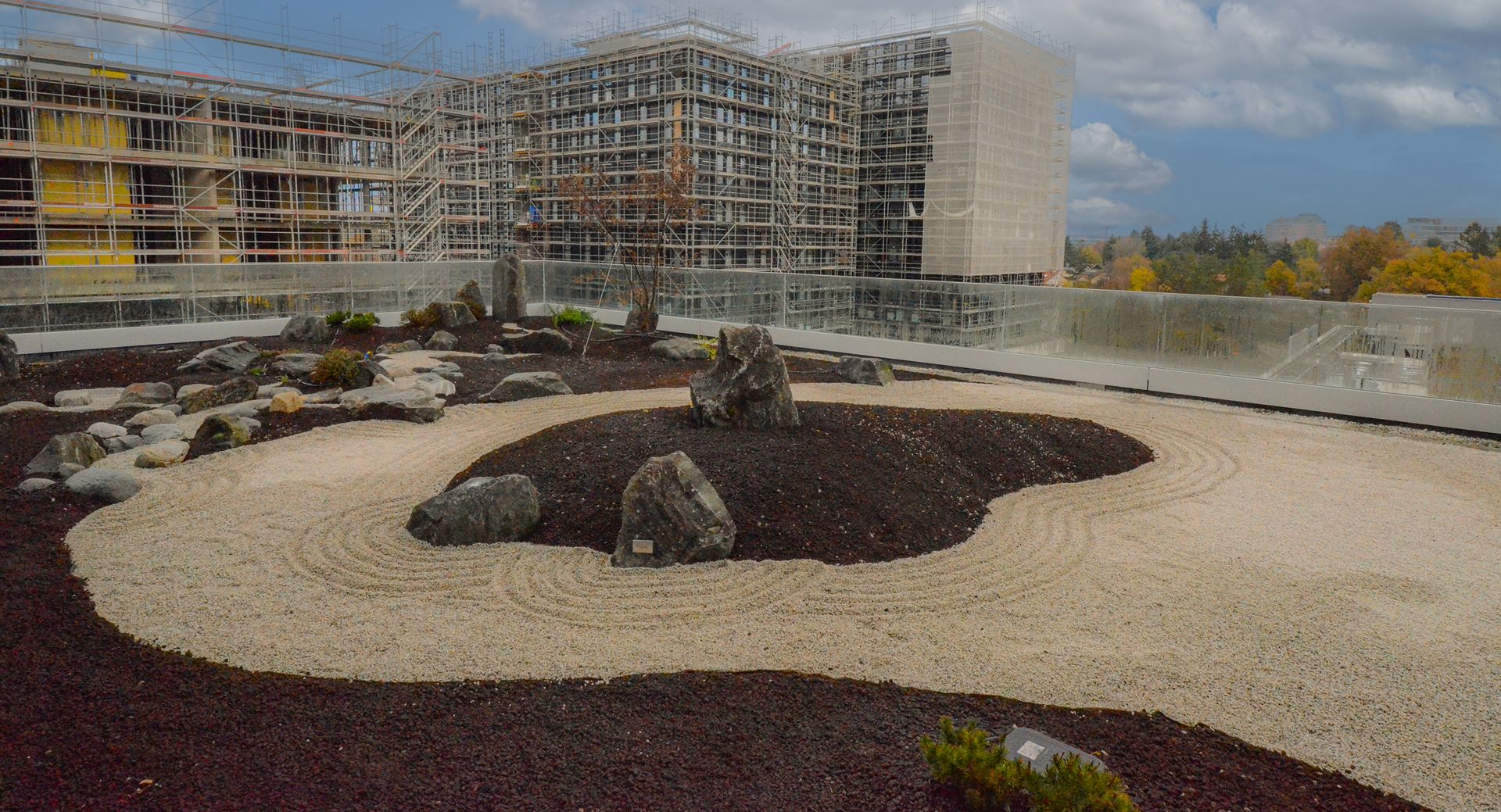 Un giardino zen su una terrazza con rocce e ghiaia di fronte a un edificio in costruzione