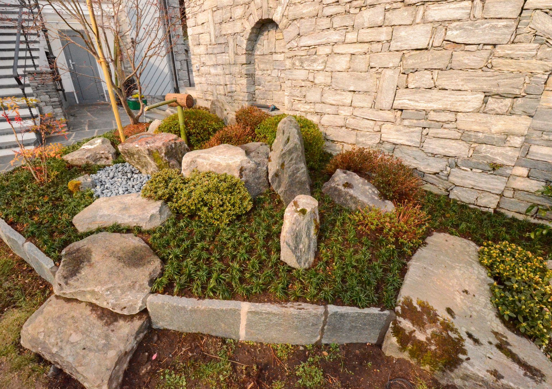 Un giardino con rocce e piante di fronte a un muro di pietra.