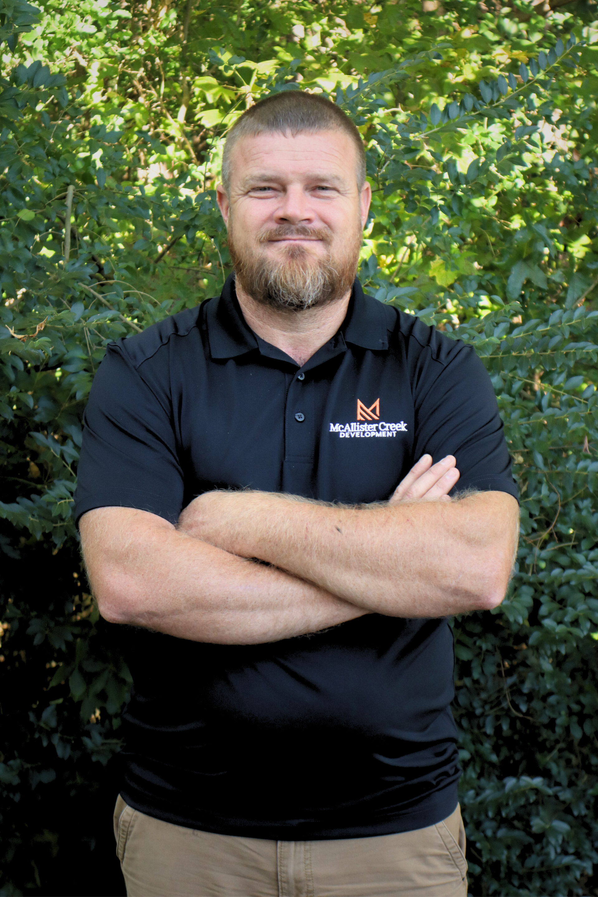 man smiling in front of tree with arms crossed