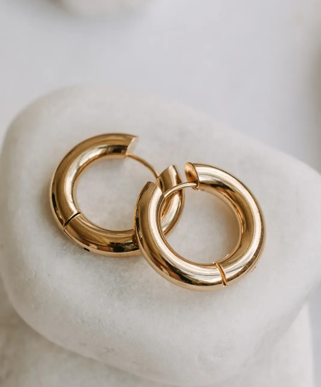 Gold hoop earrings resting on a white cushion.