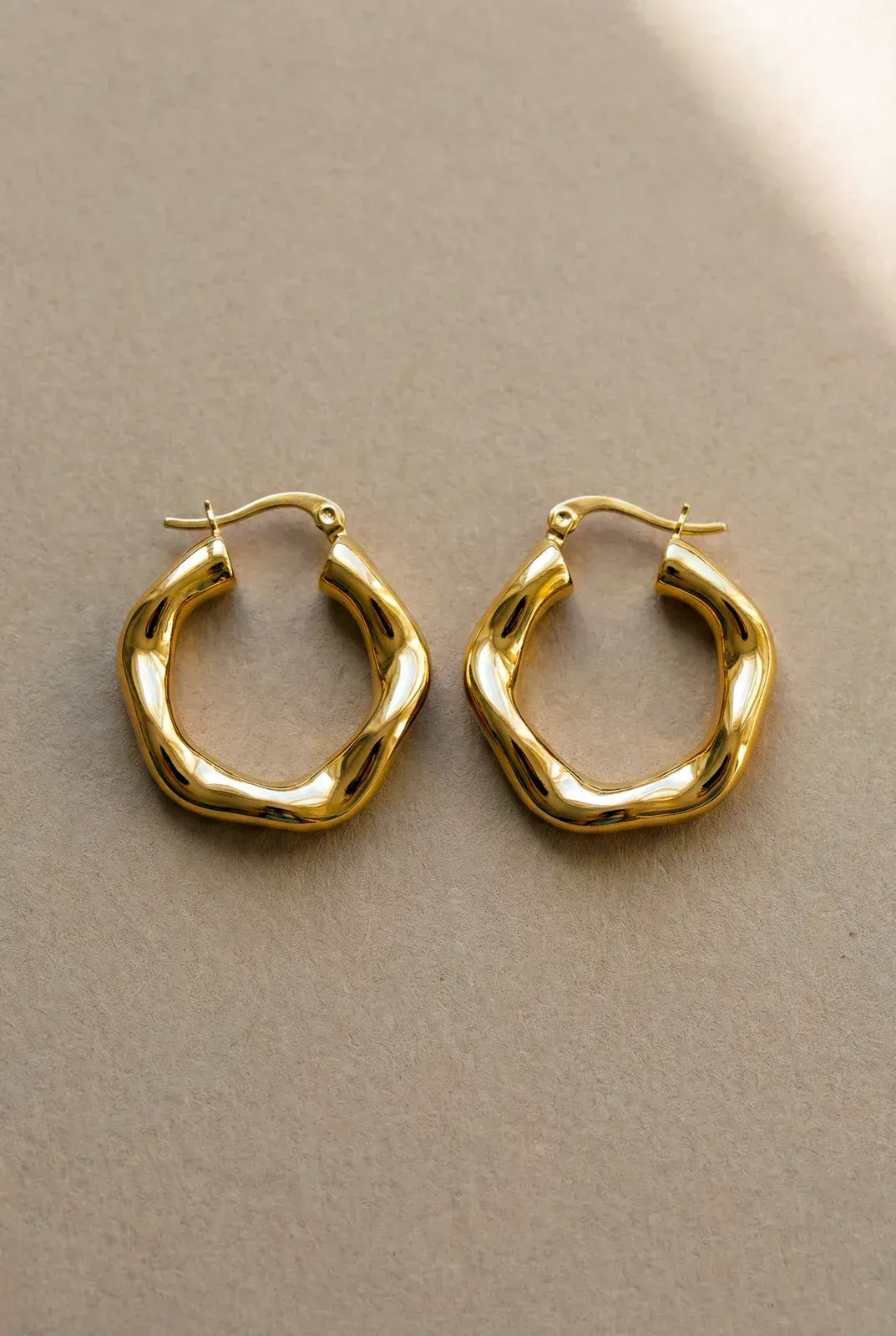 Pair of gold hoop earrings on a beige surface
