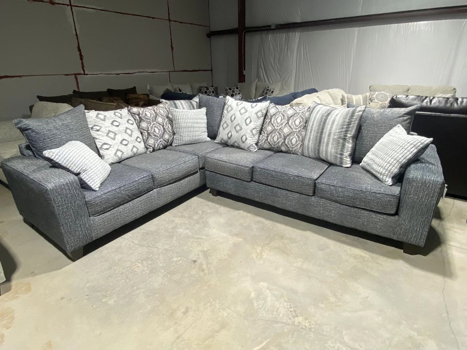 Gray sectional sofa with patterned throw pillows in a warehouse setting.