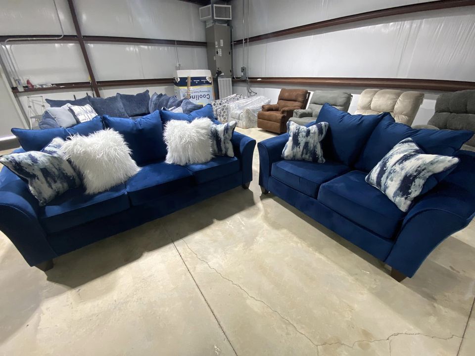 Two blue velvet sofas with pillows in a warehouse setting.