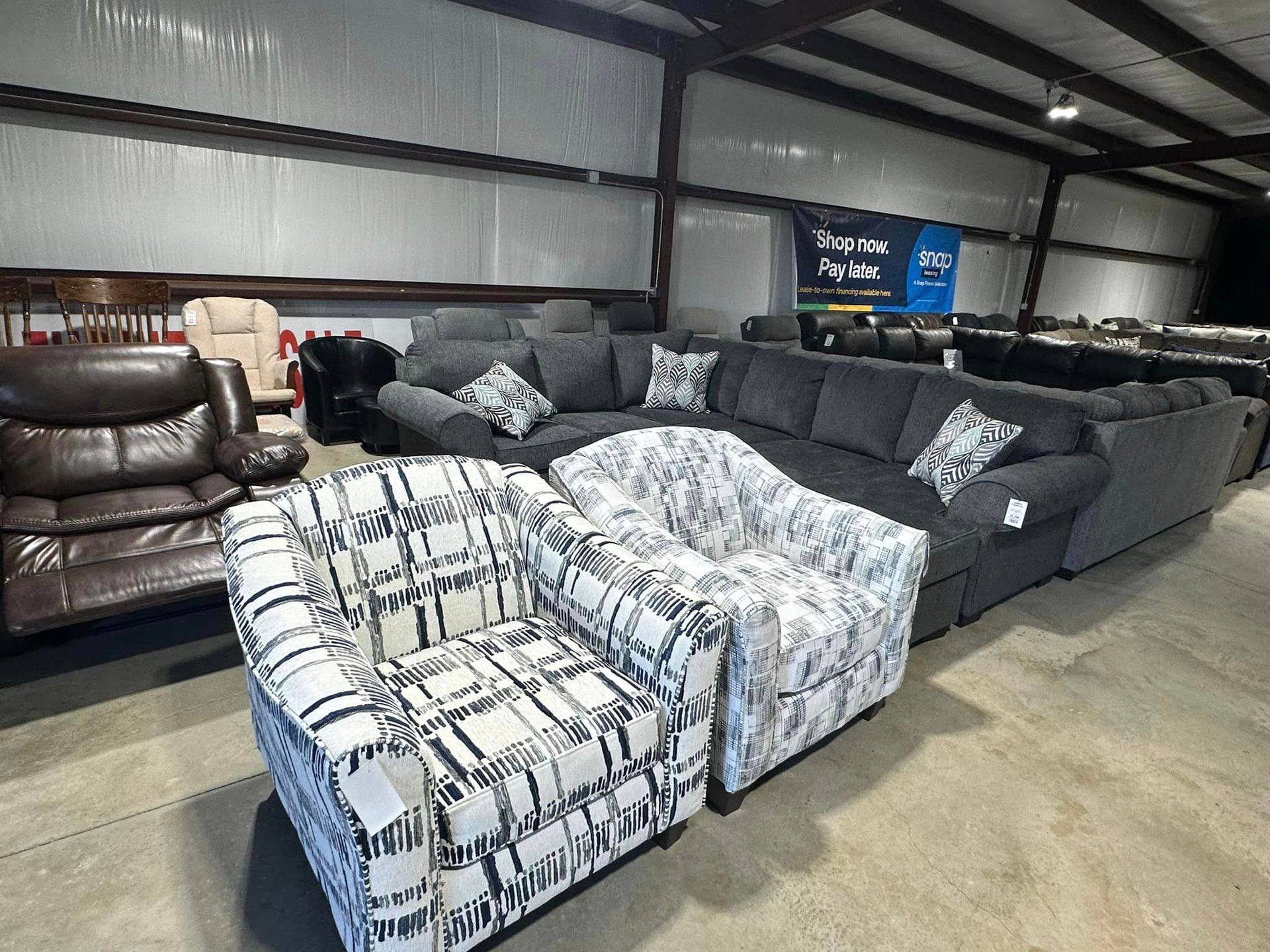 A warehouse filled with lots of furniture including a sectional couch and chairs.