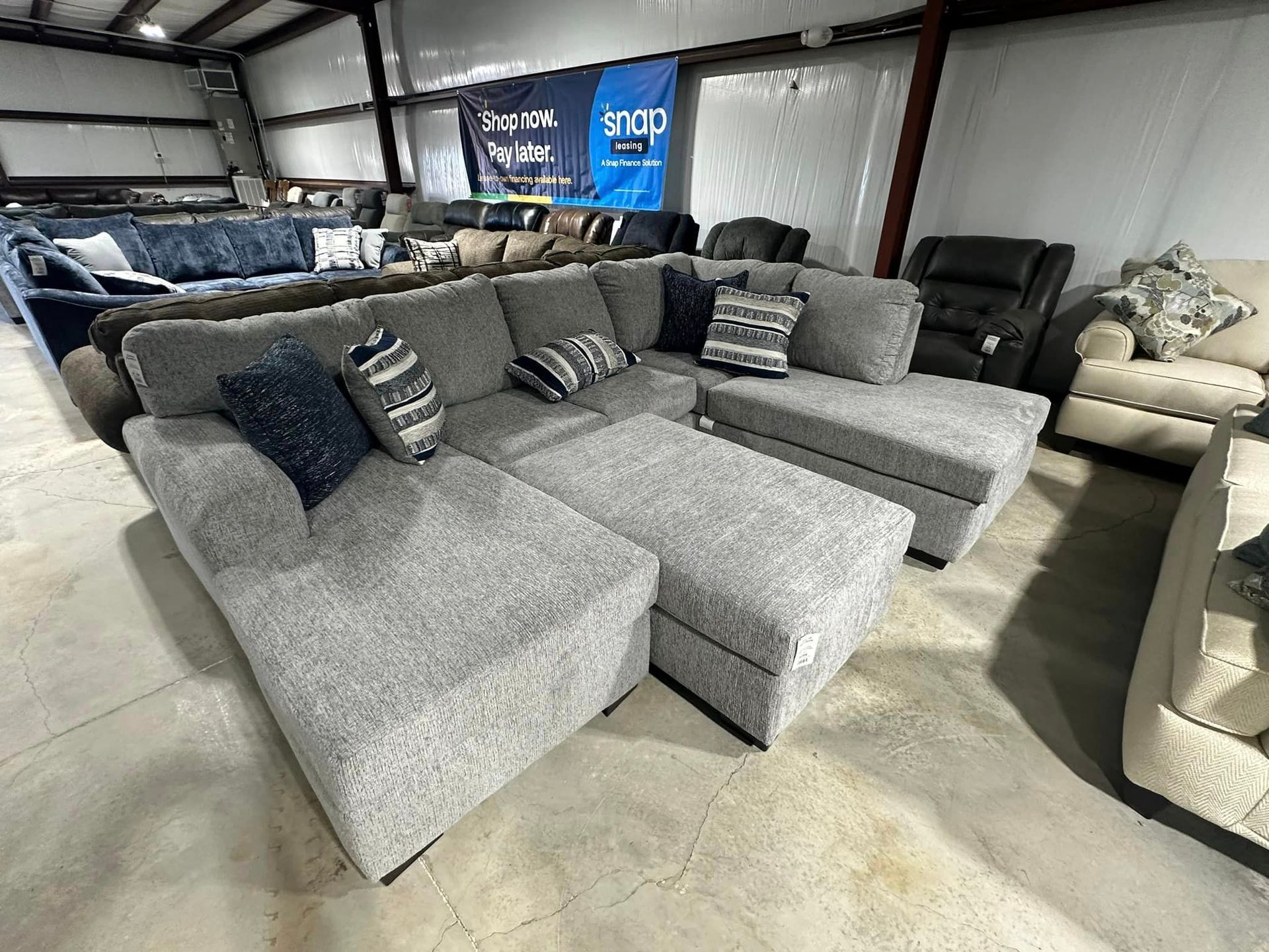 A large sectional couch is sitting in a warehouse surrounded by other furniture.