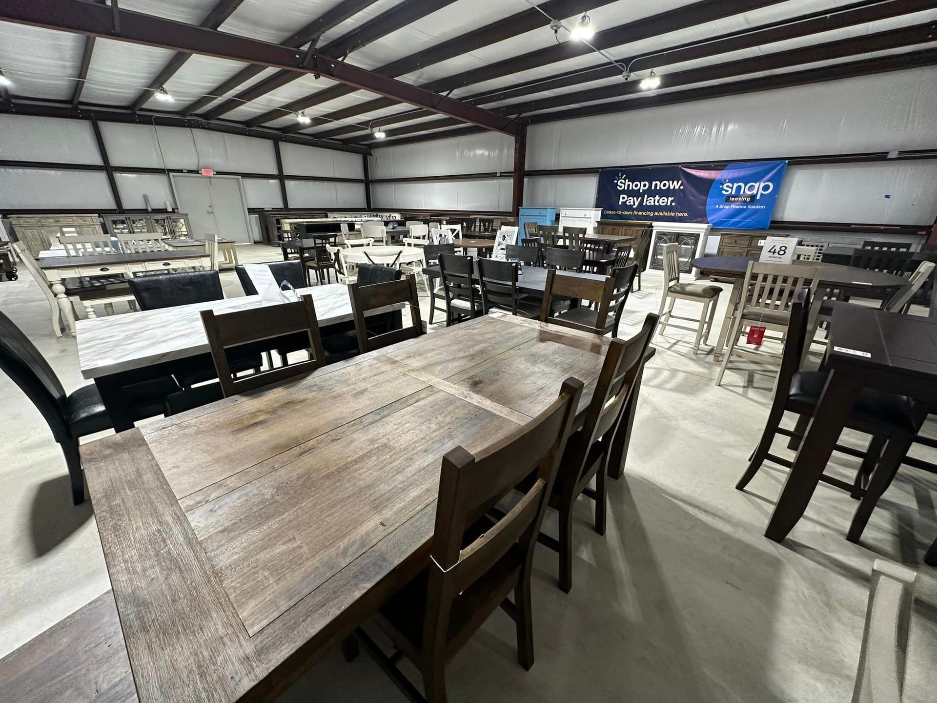 Furniture showroom with dining tables and chairs displayed under warehouse-style lighting