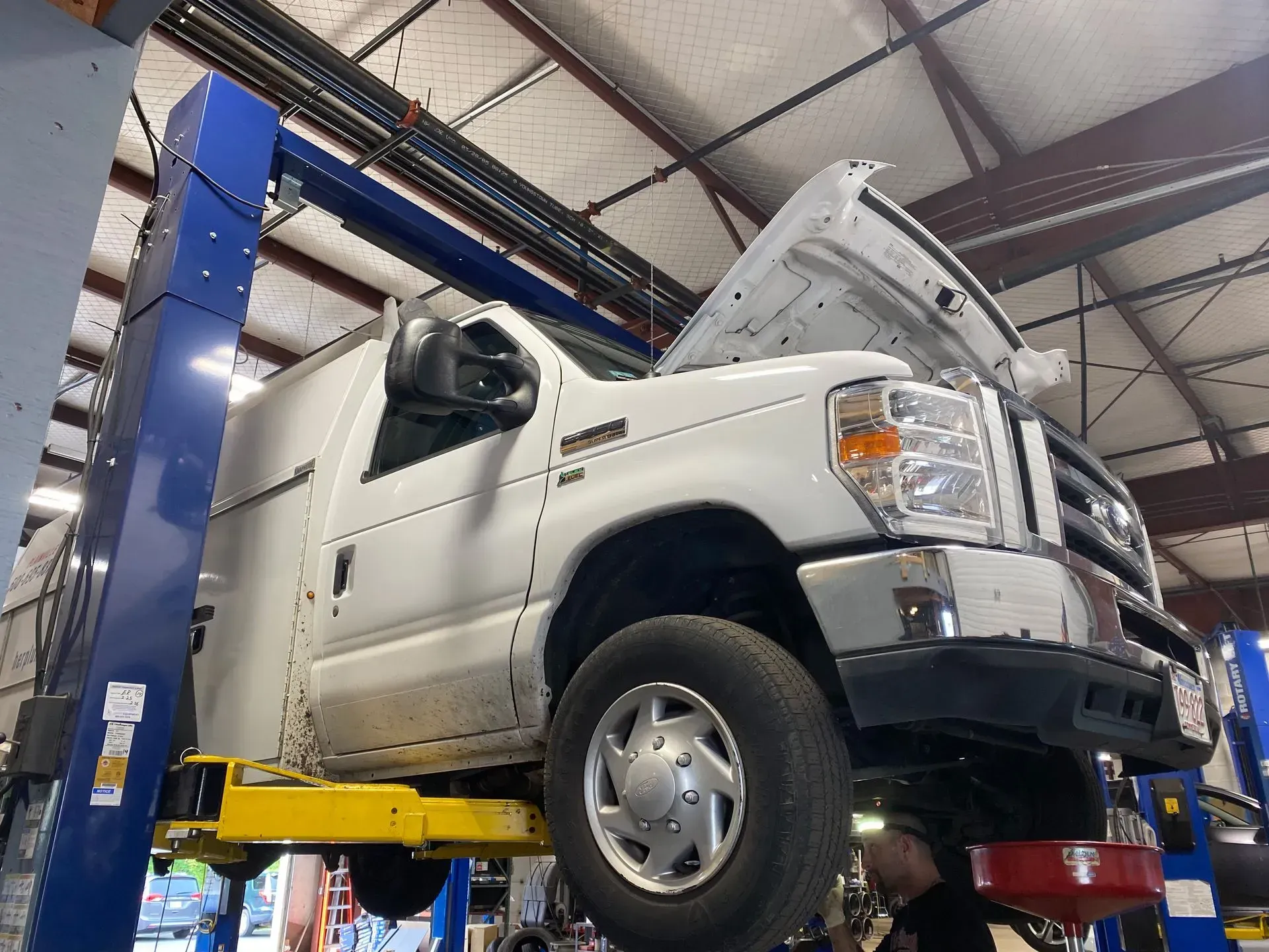 White pickup truck raised on a lift in an auto repair garage, hood open for service
